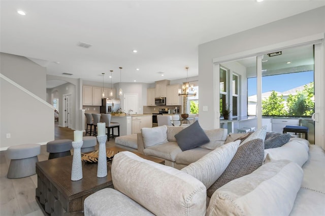 living room featuring sink, a notable chandelier, and light wood-type flooring