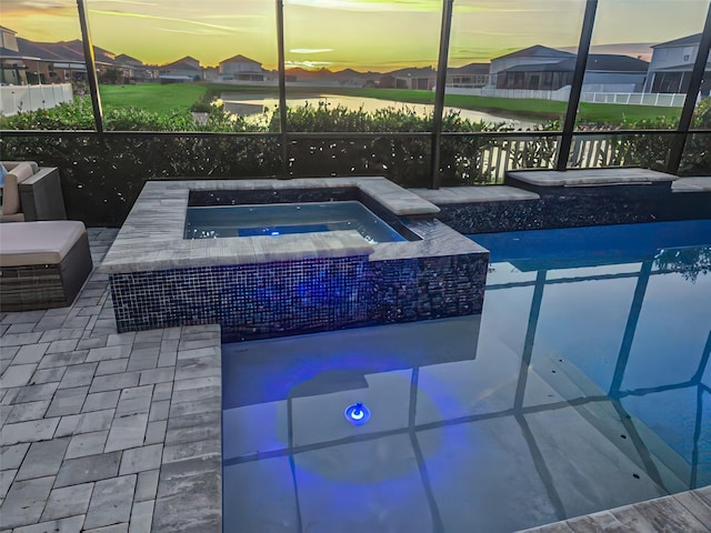 pool at dusk featuring a patio area, an in ground hot tub, and glass enclosure