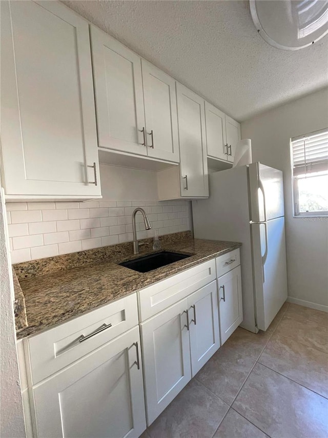 kitchen featuring sink, a textured ceiling, white cabinetry, dark stone countertops, and decorative backsplash