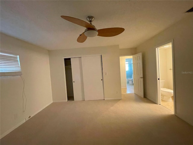 unfurnished bedroom with a closet, ensuite bathroom, light colored carpet, and ceiling fan