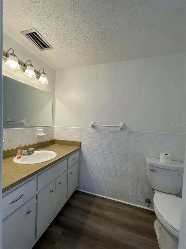 bathroom with toilet, hardwood / wood-style floors, vanity, and tile walls