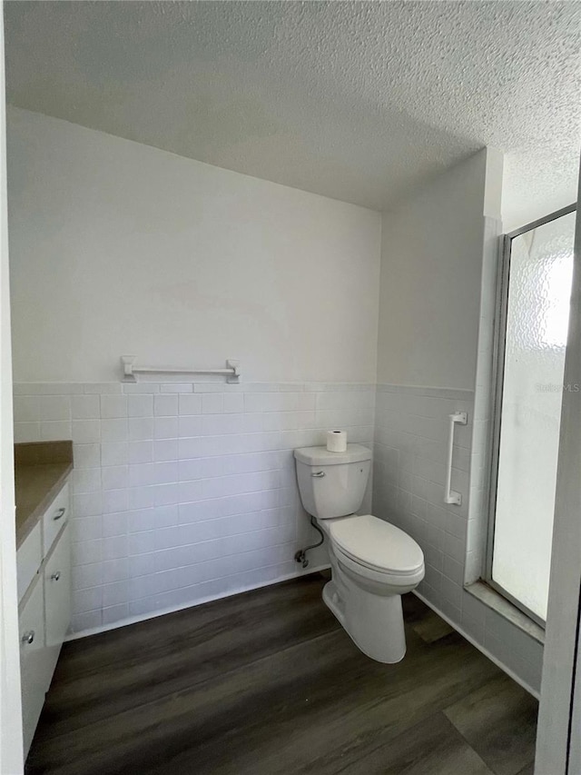 bathroom with a textured ceiling, walk in shower, wood-type flooring, toilet, and vanity