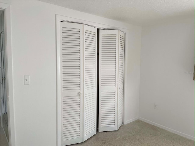 unfurnished bedroom with a closet, light carpet, and a textured ceiling