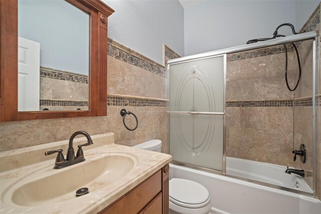 full bathroom featuring vanity, toilet, tile walls, and shower / bath combination with glass door