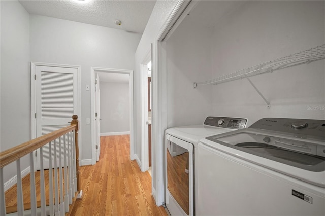 laundry area with a textured ceiling, washer and clothes dryer, and light wood-type flooring