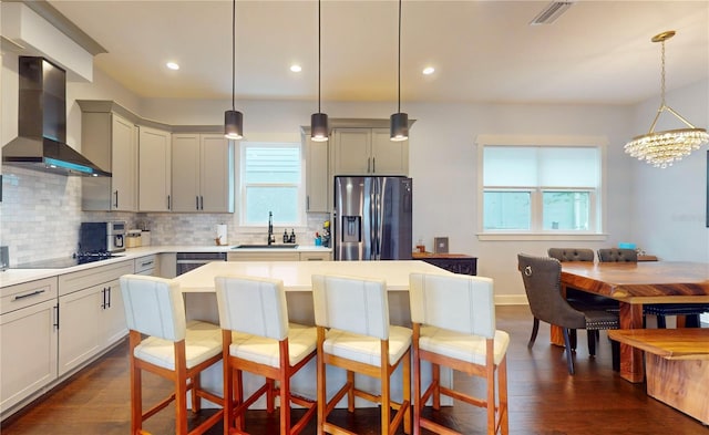 kitchen featuring wall chimney range hood, stainless steel appliances, hanging light fixtures, and dark hardwood / wood-style flooring