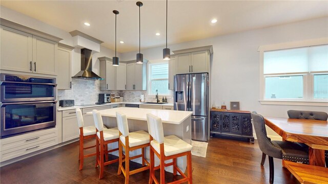 kitchen with tasteful backsplash, appliances with stainless steel finishes, wall chimney exhaust hood, decorative light fixtures, and dark wood-type flooring