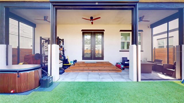 view of exterior entry with ceiling fan, a yard, a hot tub, a patio area, and french doors