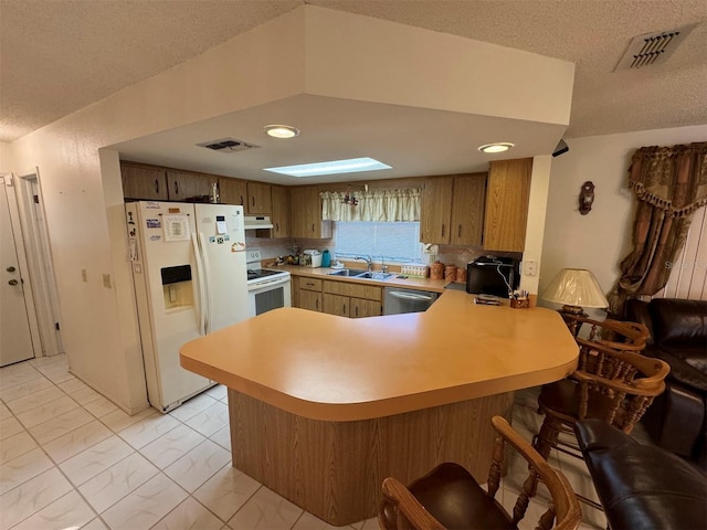 kitchen featuring a textured ceiling, white appliances, kitchen peninsula, and sink