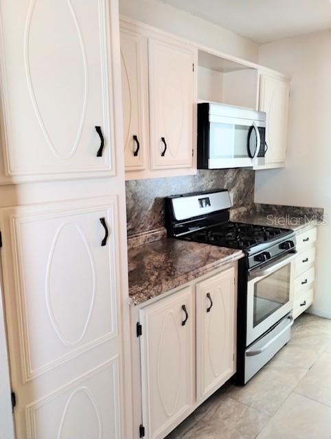 kitchen with appliances with stainless steel finishes, dark stone counters, white cabinets, and tasteful backsplash