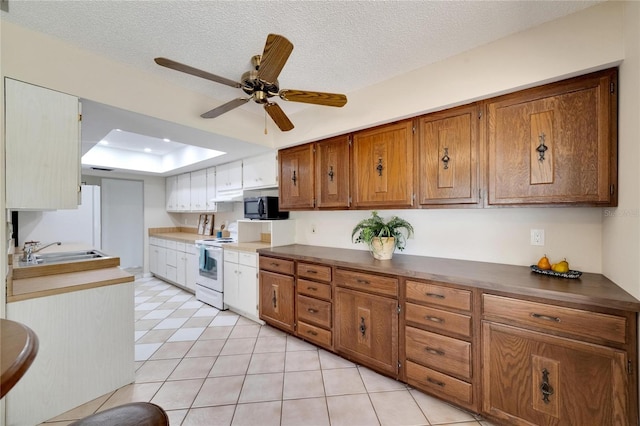 kitchen featuring ceiling fan, sink, a raised ceiling, a textured ceiling, and light tile patterned floors