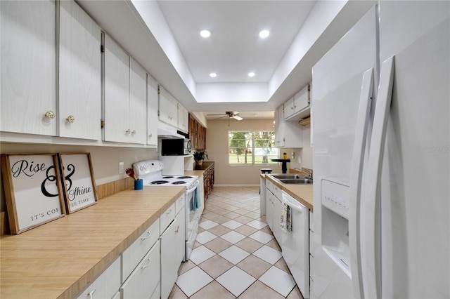 kitchen with white cabinetry, sink, white appliances, a tray ceiling, and light tile patterned flooring