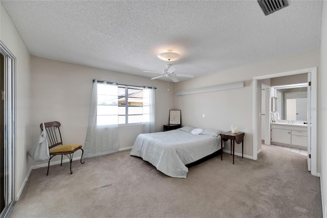 bedroom with ceiling fan, ensuite bathroom, light carpet, and a textured ceiling