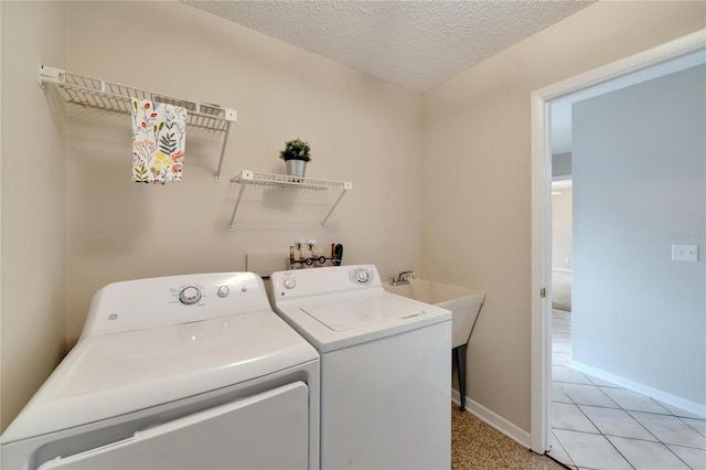 clothes washing area with a textured ceiling, washing machine and dryer, and light tile patterned flooring