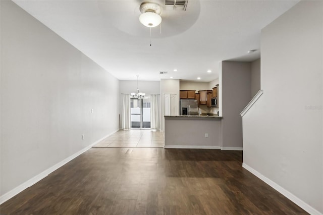 unfurnished living room with ceiling fan with notable chandelier and dark hardwood / wood-style flooring