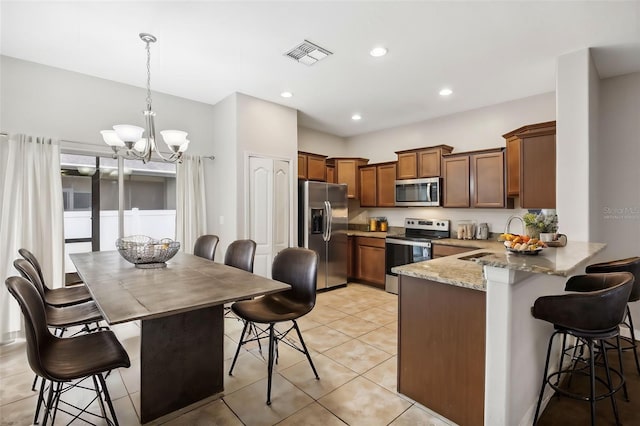 kitchen featuring kitchen peninsula, hanging light fixtures, appliances with stainless steel finishes, a kitchen breakfast bar, and light stone counters