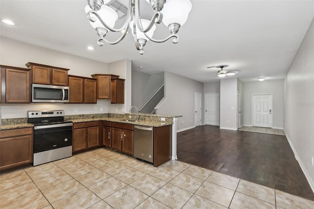 kitchen with sink, ceiling fan with notable chandelier, stone countertops, stainless steel appliances, and light hardwood / wood-style flooring