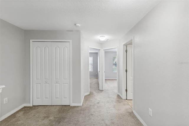 corridor featuring a textured ceiling and light colored carpet