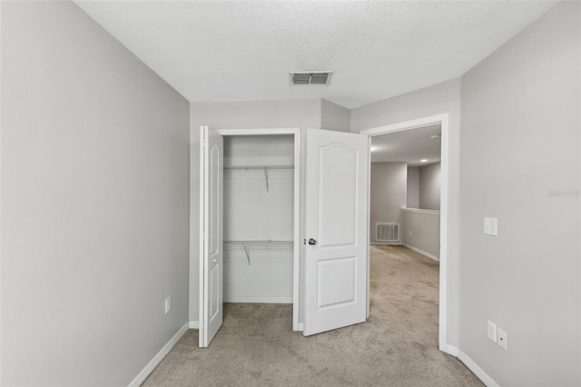 unfurnished bedroom with a textured ceiling, light colored carpet, and a closet