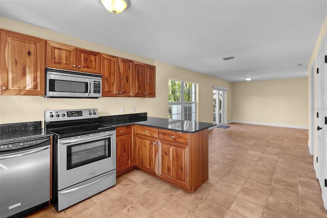 kitchen with a textured ceiling, kitchen peninsula, stainless steel appliances, and dark stone counters