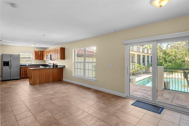 kitchen with kitchen peninsula, light tile patterned floors, a textured ceiling, and appliances with stainless steel finishes