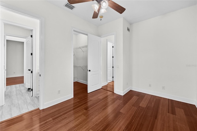 unfurnished bedroom with wood-type flooring, a walk in closet, a closet, and ceiling fan