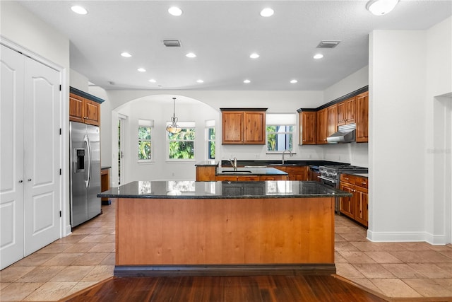 kitchen with exhaust hood, a center island with sink, dark stone countertops, and stainless steel appliances