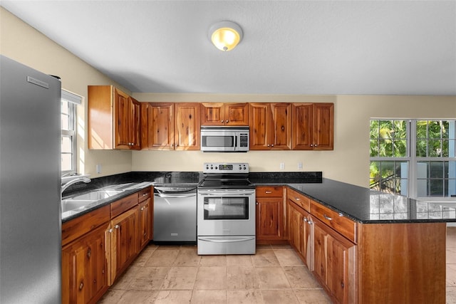 kitchen featuring kitchen peninsula, sink, appliances with stainless steel finishes, and dark stone counters