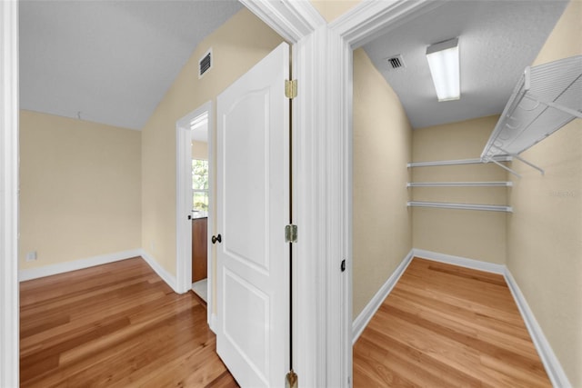 hall with wood-type flooring, a textured ceiling, and vaulted ceiling