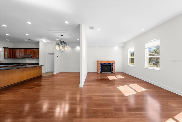 unfurnished living room featuring a tile fireplace, sink, dark wood-type flooring, and a notable chandelier