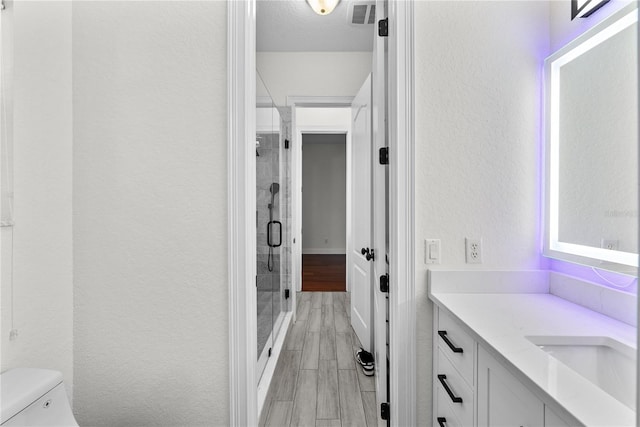 bathroom featuring wood-type flooring, a textured ceiling, toilet, a shower with door, and vanity