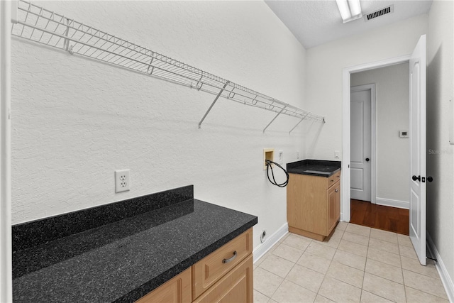 clothes washing area featuring cabinets, light tile patterned floors, a textured ceiling, and hookup for a washing machine