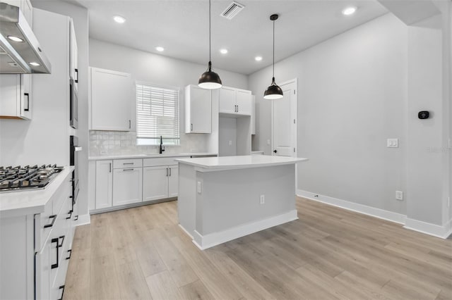 kitchen with extractor fan, decorative light fixtures, white cabinets, light hardwood / wood-style floors, and stainless steel gas stovetop