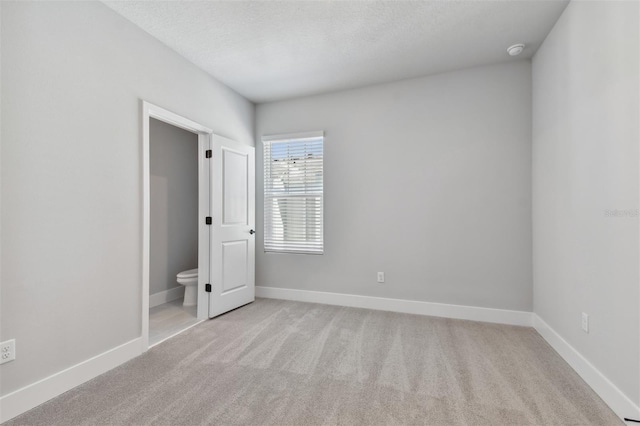 unfurnished bedroom featuring ensuite bathroom, light colored carpet, and a textured ceiling