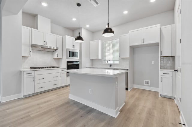 kitchen with white cabinets, pendant lighting, stainless steel appliances, and light hardwood / wood-style floors