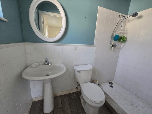 bathroom with a tile shower, hardwood / wood-style flooring, toilet, and tile walls