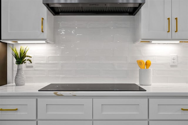 interior details featuring white cabinetry, light stone counters, exhaust hood, and black electric stovetop