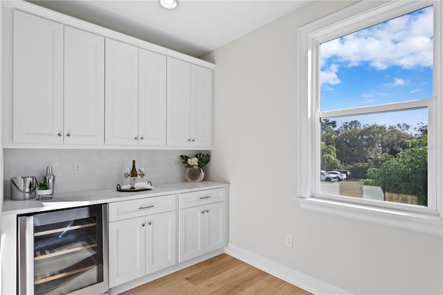 bar with white cabinets, backsplash, light hardwood / wood-style floors, and beverage cooler