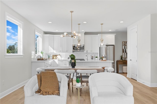 kitchen with white cabinetry, stainless steel appliances, pendant lighting, decorative backsplash, and a center island with sink