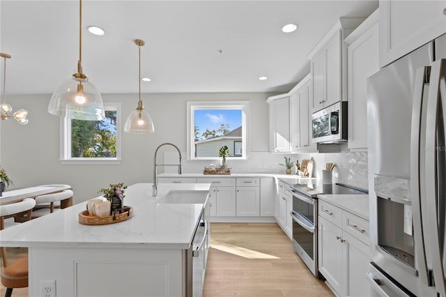 kitchen featuring appliances with stainless steel finishes, sink, a center island with sink, decorative light fixtures, and white cabinetry