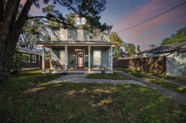 back house at dusk featuring covered porch and a lawn