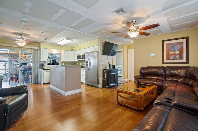 living room featuring light hardwood / wood-style floors, a textured ceiling, and ceiling fan