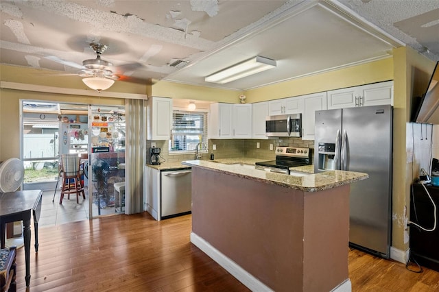 kitchen featuring a healthy amount of sunlight, stainless steel appliances, white cabinetry, and wood-type flooring