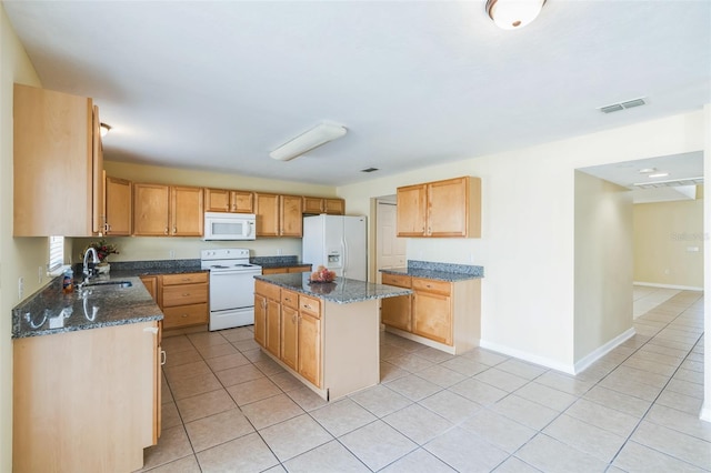 kitchen with white appliances, light tile patterned flooring, sink, a kitchen island, and dark stone countertops