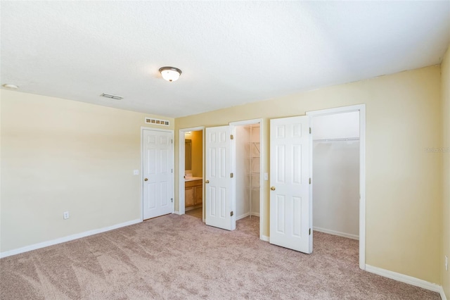 unfurnished bedroom with light carpet, a walk in closet, and ensuite bath