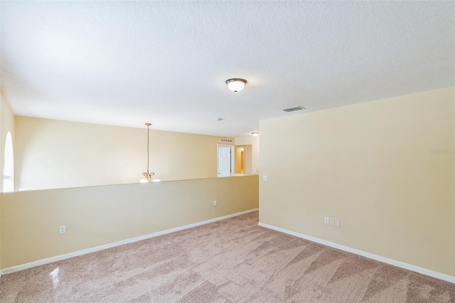 spare room with a notable chandelier, a textured ceiling, and light colored carpet