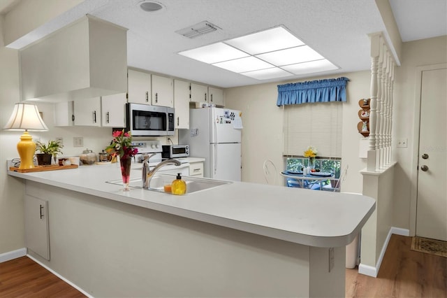 kitchen with sink, white refrigerator, kitchen peninsula, light hardwood / wood-style floors, and white cabinets