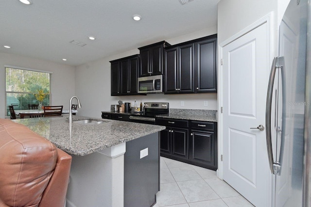 kitchen featuring an island with sink, stainless steel appliances, sink, light stone countertops, and light tile patterned flooring