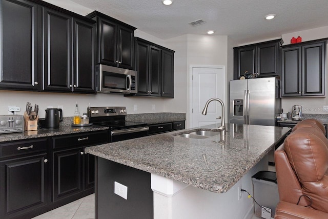 kitchen featuring an island with sink, appliances with stainless steel finishes, a breakfast bar area, a textured ceiling, and sink