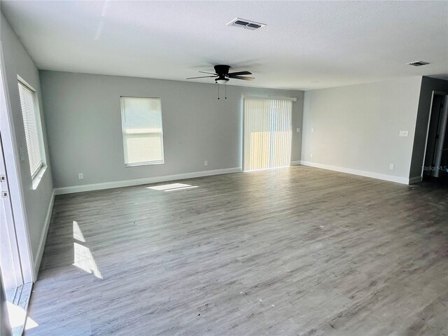 empty room with baseboards, a ceiling fan, wood finished floors, and visible vents